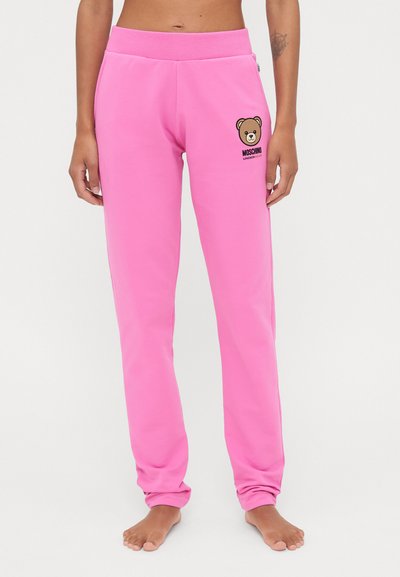 Pantalon de survêtement rose avec une taille côtelée, arborant un graphique d'ours et le texte "MOSCHINO" sur la cuisse gauche. Fabriqué en matériau doux en mélange de coton.