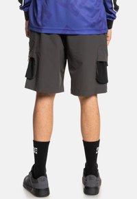 Grijze cargoshorts met zijzakken, gecombineerd met zwarte crew-sokken en grijze schoenen. De stof lijkt lichtgewicht en gestructureerd te zijn.