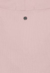 Zart rosa Stoff mit einem kleinen runden Metallknopf, der mit unleserlichem Text geprägt ist, nahe einer genähten Naht.
