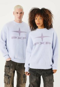 Maglioni pelosi azzurro chiaro con logo "PXP" lavanda e design a stella. Indossati con pantaloni scuri in stile cargo caratterizzati da tasche e cerniere.