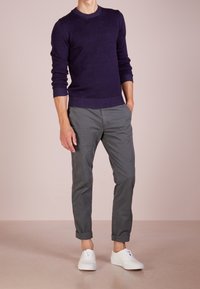 Pull en maille bleu marine avec un col rond, associé à un pantalon chino gris retroussé et des baskets blanches, créant une tenue décontractée.