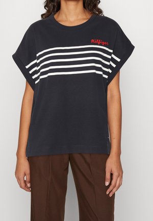 Mørkeblå t-shirt med brede, korte ærmer, der har hvide vandrette striber og rød "Hilfiger" broderi på brystet. Blødt, bomuldsstof.