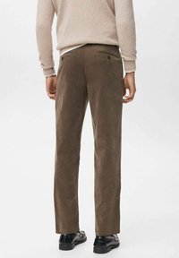 Pantalones de pana marrones con corte recto, que cuentan con dos bolsillos traseros y una textura suave, combinados con zapatos negros.