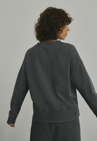 Grå sweatshirt lavet af blødt stof, med en afslappet pasform, sænkede skuldre, ribbet halsudskæring og manchetter.