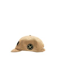 Gorra color caqui de tela, con visera curvada, correa ajustable y un parche circular negro con texto y diseño en amarillo en la parte frontal.