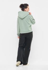Felpa con cappuccio verde menta, dal fit rilassato, con polsini a coste e tasca a marsupio, abbinata a pantaloni neri larghi e calzature leggere.