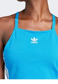 Blå atletisk linne med tunna axelband, med en Adidas-logotyp i vitt. Slät textur med en åtsittande design och kontrasterande sidostrickor.