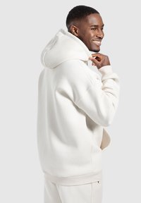 Sudadera con capucha de color crema, mezcla de algodón suave, que cuenta con una gran capucha, puños acanalados y bolsillos laterales, con un diseño de corte relajado.