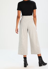 High-waisted, wide-leg trousers in a striped beige and white pattern, paired with a fitted black t-shirt and black heeled ankle boots.
