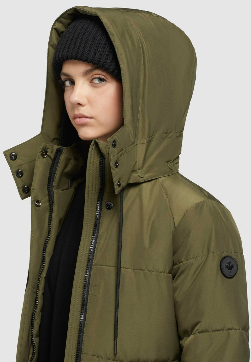 Olivgrüne Steppjacke mit Kapuze, ausgestattet mit Reißverschluss- und Druckknopfverschlüssen, schwarzen Akzenten und einem runden Logo auf dem linken Ärmel. Strukturierter Stoff.