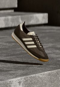 Ruskea lenkkari, jossa beigejä raitoja ja yksityiskohtia, mokkanahkaa ja verkkokangasta, pyöreä kärki, kumipohja ja näkyvä nauhoitusjärjestelmä.