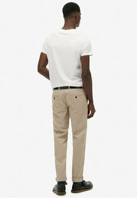 Pantalones beige con puños doblados, bolsillos cosidos y un cinturón de cuero negro; combinados con una camiseta blanca de manga corta y lisa.