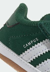 Zelene semišne teniske z belimi usnjenimi črtami, teksturiranimi dodatki in gumo gumijastim podplatom; označene z "CAMPUS" v belem tisku.
