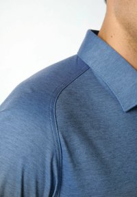 Blaues Poloshirt aus strukturiertem Stoff, mit klassischem Kragen und subtilen Schattierungen. Nahaufnahme, die das Detail von Schulter und Kragen einfängt.