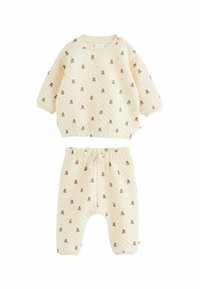 Quiltet to-dels babytøj i creme, med et mønster af små brune krammedyr. Toppen har en rund hals; bukser med elastisk talje.