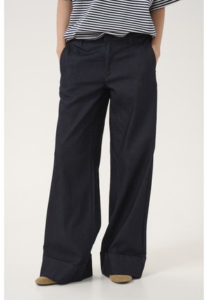 Pantalones de mezclilla oscuros de pierna ancha con una textura suave, que cuentan con un pliegue frontal, bolsillos laterales y puños doblados. Se combinan con una camiseta a rayas.