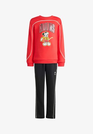 Un sweat rouge présente un logo Adidas et un graphique de Mickey Mouse ; assorti à un pantalon noir avec des rayures blanches sur les côtés et un logo Adidas.
