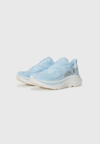 Light blue running shoes with a breathable mesh upper, thick white sole, and reflective silver logo on the side. Low-top design with laces.