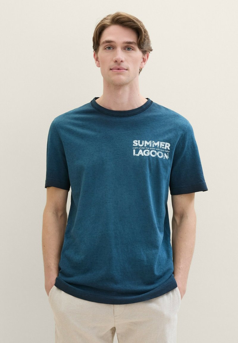 Dark teal cotton t-shirt with short sleeves, ribbed crew neck, and white printed text "SUMMER LAGOON" on the chest. Side seam details visible.
