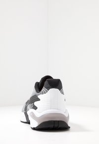 Scarpa sportiva bianca e nera con tomaia in maglia testurizzata, tacco arrotondato e suola ammortizzata con dettagli in gomma.