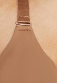 Cinghietto di reggiseno marrone con una superficie liscia e testurizzata e un regolatore in metallo, collegato a una coppa di reggiseno morbida e triangolare.