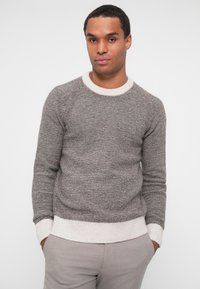 Sweater cinza com gola e punhos em creme com textura canelada, apresentando riscas horizontais. O material parece suave e texturizado. Combinado com calças claras.