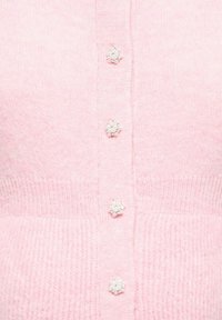 Jasnoróżowy kardigan wykonany z miękkiego dzianinowego materiału, ozdobiony guzikami w kształcie kwiatów z perłowymi detalami. Prążkowana faktura na dole.