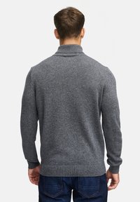 Pull en maille gris avec col montant, poignets et ourlet côtelés, porté avec un jean en denim bleu. Coupe ajustée avec une finition texturée.