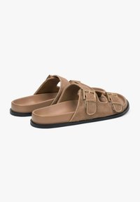 Brown fur-lined sandals with two adjustable buckle straps, a smooth tan footbed, and a black rubber outsole.