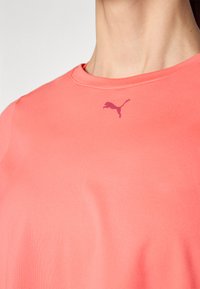 Korallfärgad sportt-shirt med rund hals, korta ärmar och en subtil rosa Puma-logotyp på bröstet. Slät, lätt tygtextur.