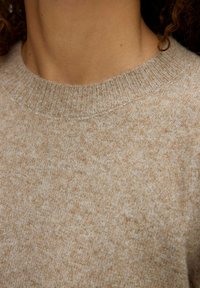 Maglione beige lavorato a maglia con finitura testurizzata, scollatura arrotondata e colletto a coste. Il materiale sembra morbido e caldo.