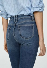 Traperice s srednjim strukom, tamnoplavim pranjem i klasičnim dizajnom s pet džepova. Sadrže dva stražnja džepa s detaljima šivanja.