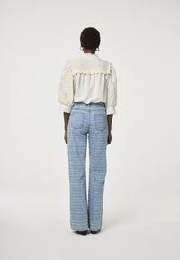 Witte blouse met geborduurde pofmouwen en een kanten rand, gecombineerd met lichtblauwe, met patronen versierde, hoge taille jeans, gezien vanaf de achterkant.