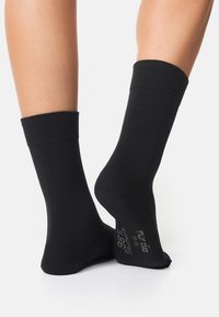 Sorte bomuldsstrømper med ribbede manchetter, ankellængde, med trykt tekst på sålen, der angiver materiale- og størrelsesoplysninger.