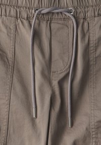 Pantalons en coton beige avec une taille élastique munie d'un cordon de serrage, œillets en métal et deux poches latérales. Texture lisse.