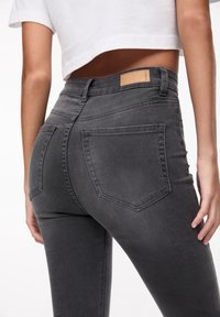 Tummanharmaat denimsiniset korkeavyötäröiset skinny-farkut, joissa on nahkalappu takana, kaksi läppätaskua ja sileä pinta.