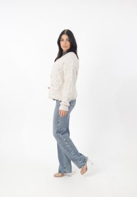 Krämfärgad, fluffig cardigan med rund halsringning och två framfickor, kombinerad med ljusblå raka jeans och klara klacksandaler.