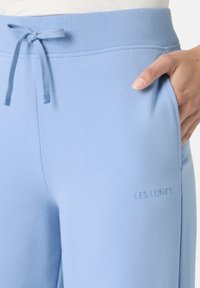 Lyseblå sweatpants lavet af blødt stof, med en snøre i taljen og sidelommer. Teksten "LES LUNES" præget nær lommen.