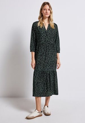 Robe midi à imprimé léopard vert avec des manches trois-quarts, volants superposés à l'ourlet, associée à des baskets neutres. Texture de tissu lisse.