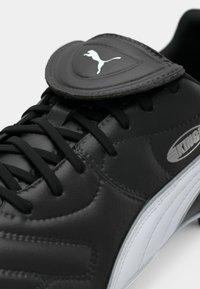 Black leather Puma King soccer cleat showing laces, stitched details, and white Puma logo on fold-over tongue.