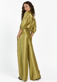 Metallic olijfgroene satijnen set met een blouse met pofmouwen en brede broek met zijzakken en een gladde textuur.