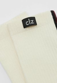Krämfärgade ribbade strumpor med en svart etikett som har texten "clz", med en slät textur och ett subtilt mönster vid kragen.