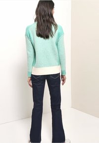 Vaaleanvihreä ribbineulepaita, jossa on kermaiset virheet, yhdistetty tummansinisiin liehuhousuihin. Pehmeä tekstuuri, rento istuvuus ja minimalistinen yksityiskohtaisuus.