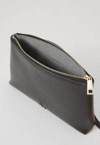 Pochette zippée en cuir noir avec une texture lisse, quincaillerie zippée dorée et doublure intérieure rayée. Forme rectangulaire compact pour le rangement.