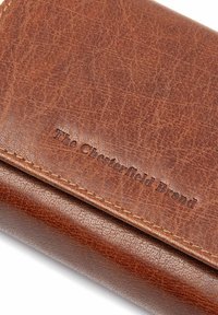 Billetera de cuero marrón con un acabado texturizado y el logo en relieve "The Chesterfield Brand", con costuras sutiles y bordes suaves.