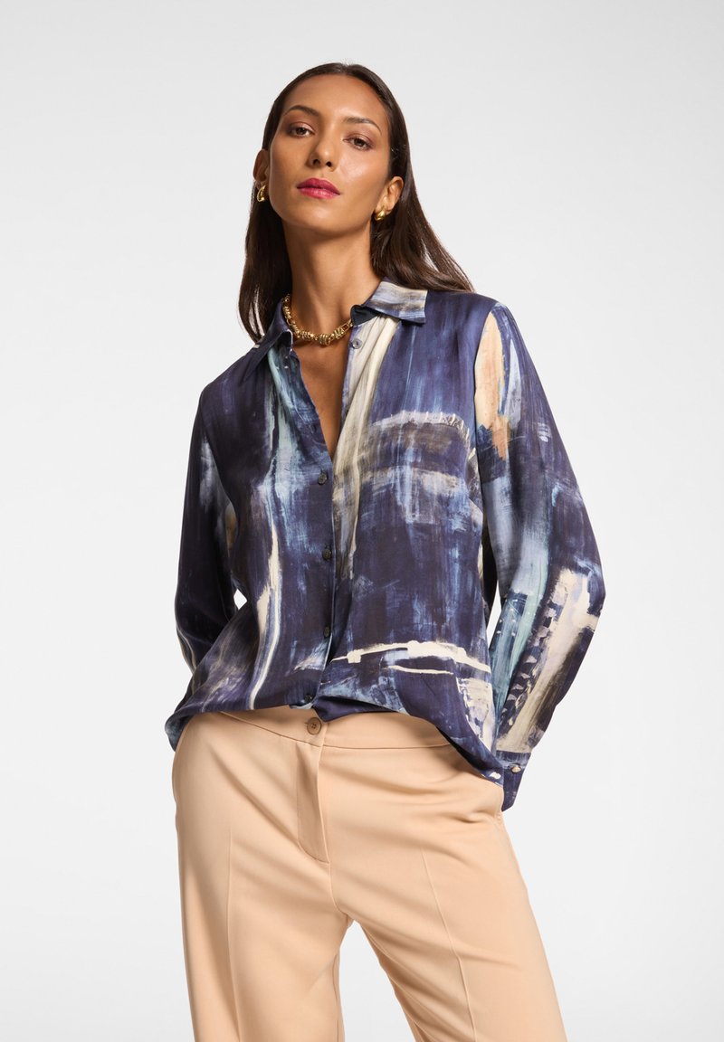 Camicia a maniche lunghe con bottoni di colore blu scuro, decorata con motivi astratti in crema e blu chiaro. Tessuto satinato con vestibilità rilassata e colletto.