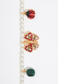 Il braccialetto di perle presenta charm in tonalità oro: una coccinella rossa e nera, una farfalla con strass multicolori e una pietra verde scuro.