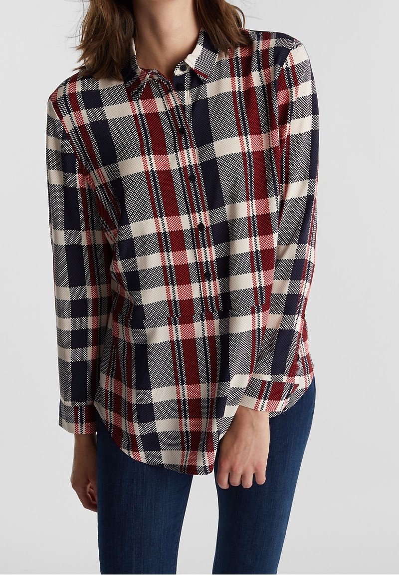 Donna che indossa una camicia a maniche lunghe con motivo a quadri rosso, blu navy e bianco e jeans blu scuro.