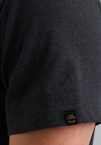 Čierne tričko s krátkym rukávom z mäkkej látky, s výraznou značkou na rukáve a čistým, klasickým strihom.