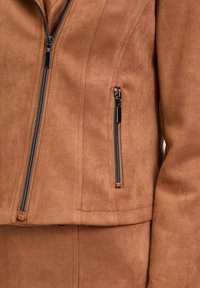 Brown faux suede jacket with a fitted design, featuring zippered pockets, silver zipper hardware, and smooth texture.